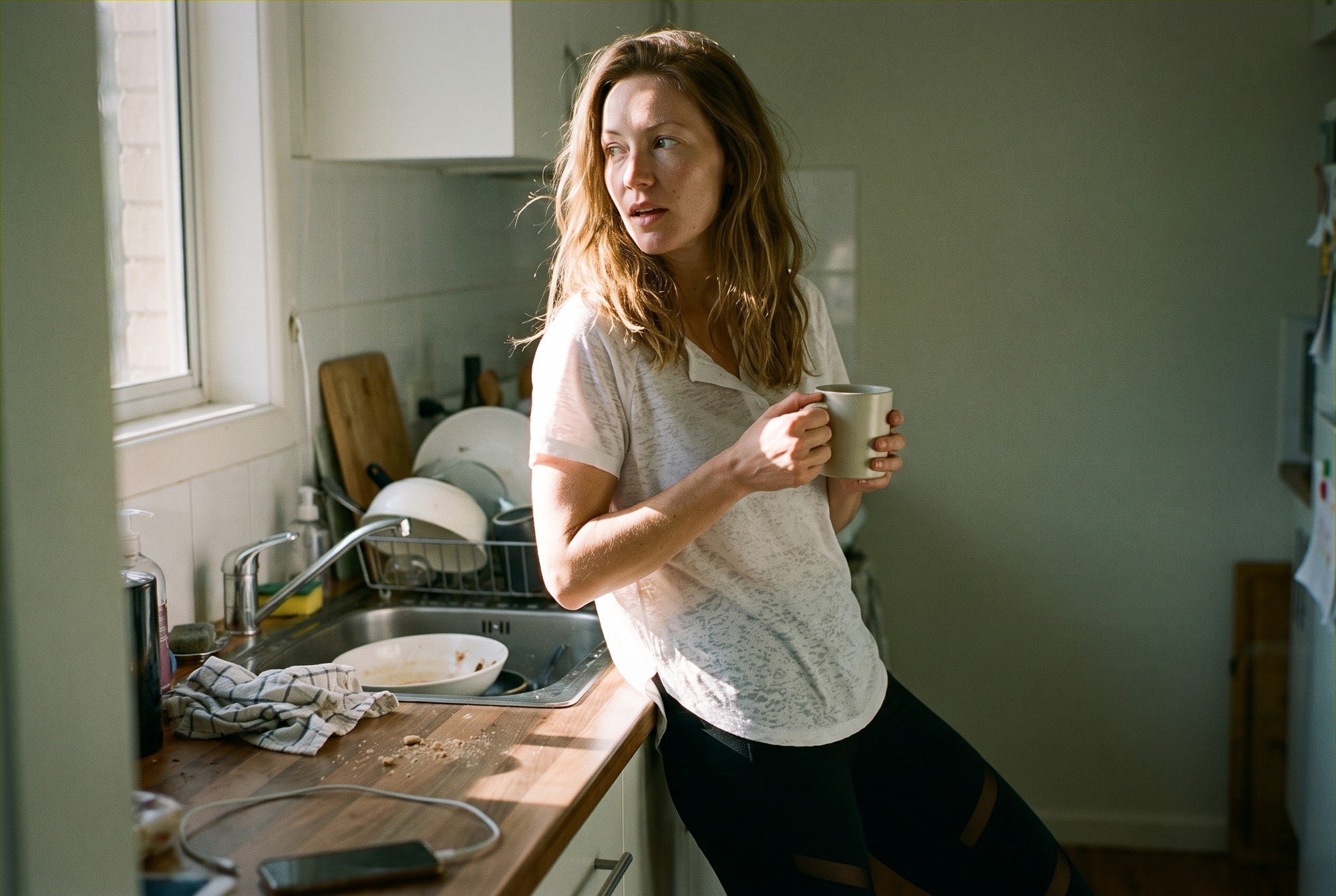 Woman at home on a rest day morning in the RYZ Original Breeze Relaxed Tee in white over Core Mesh-Slit Leggings in black, holding a mug in low morning light